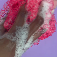Load and play video in Gallery viewer, A video of a pink sudsy exfoliating sponge scrubbing an arm in front of a lilac background.