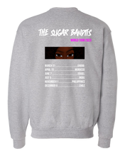 Load image into Gallery viewer, The back of a heather gray crewneck sweater has The Sugar Bandits written horizontally in white at the top and World Tour 2023 written in hot pink centered under the word Bandit. There is an image of just The Sugar Bandits Bandit’s eyes centered underneath and below that are the tour dates and places they’ll visit on the tour. 
