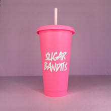 Load image into Gallery viewer, A hot pink plastic cup with a lid and straw that looks like a fast food cup is on a baby pink background. It has the The Sugar Bandits logo in white written in the center of the cup.
