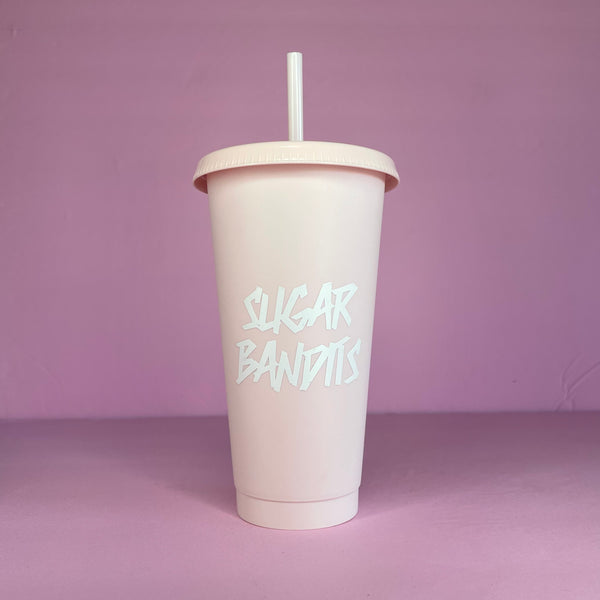 A rose blush plastic cup with a lid and straw that looks like a fast food cup is on a baby pink background. It has the The Sugar Bandits logo in white written in the center of the cup.