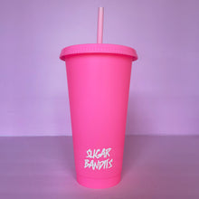 Load image into Gallery viewer, A hot pink plastic cup with a lid and straw that looks like a fast food cup is on a baby pink background. It has the The Sugar Bandits logo written in white at the bottom of the cup.
