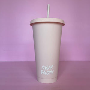 A rose blush plastic cup with a lid and straw that looks like a fast food cup is on a baby pink background. It has the The Sugar Bandits logo written in white at the bottom of the cup.