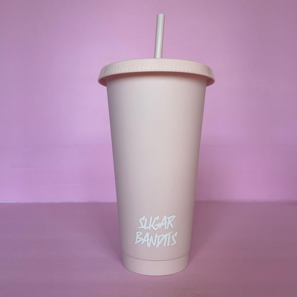 A rose blush plastic cup with a lid and straw that looks like a fast food cup is on a baby pink background. It has the The Sugar Bandits logo written in white at the bottom of the cup.